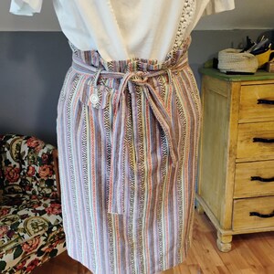 May include: A high-waisted skirt featuring a multi-colored vertical striped pattern with geometric motifs, a gathered elasticized waistband, and a matching fabric tie belt, paired with a white short-sleeved top with lace trim details.
