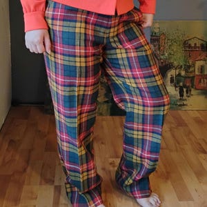 May include: Plaid pants in red, yellow, green, and blue. The pants are paired with a long-sleeved orange shirt. The plaid pattern is a classic design, suitable for casual wear. The pants are made of a soft, comfortable material.