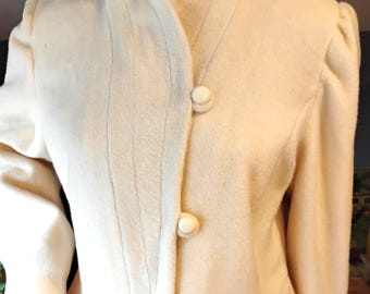 Pode incluir: Casaco vintage creme com gola alta e três botões grandes e redondos. O casaco apresenta um corte sob medida com detalhes de costura sutis e mangas ligeiramente bufantes, sugerindo um estilo retrô clássico.
