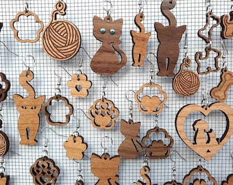 May include: A variety of wooden cat-themed earrings, including paw prints, cats, yarn balls, and hearts. The earrings are displayed on a wire grid.