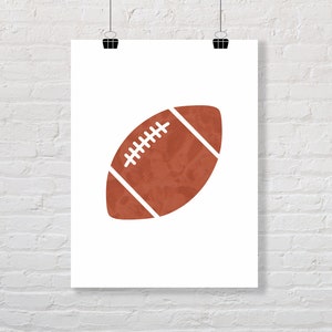 Puede incluir: Una ilustraci&oacute;n de una pelota de f&uacute;tbol marr&oacute;n y blanca sobre un fondo blanco. La pelota de f&uacute;tbol es una silueta simple con una apariencia texturizada.