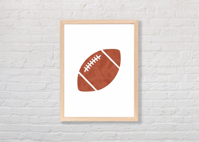 Puede incluir: Una impresi&oacute;n enmarcada de una pelota de f&uacute;tbol marr&oacute;n sobre un fondo blanco. La pelota de f&uacute;tbol es una silueta simple con costuras blancas.