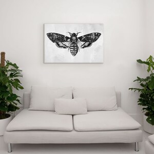 Peut inclure: Une illustration en noir et blanc d'un papillon de nuit aux grandes ailes, imprim&eacute;e sur une toile et encadr&eacute;e. La toile est accroch&eacute;e &agrave; un mur blanc au-dessus d'un canap&eacute; blanc.