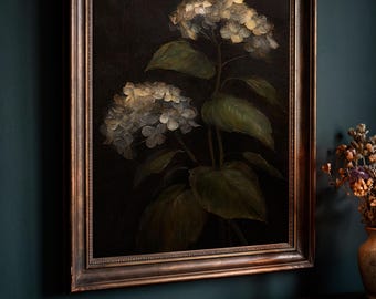 May include: A framed oil painting featuring two clusters of hydrangea flowers with muted white and pale blue petals, set against a dark, moody background. The artwork is encased in a dark, ornate, metallic-toned wooden frame.