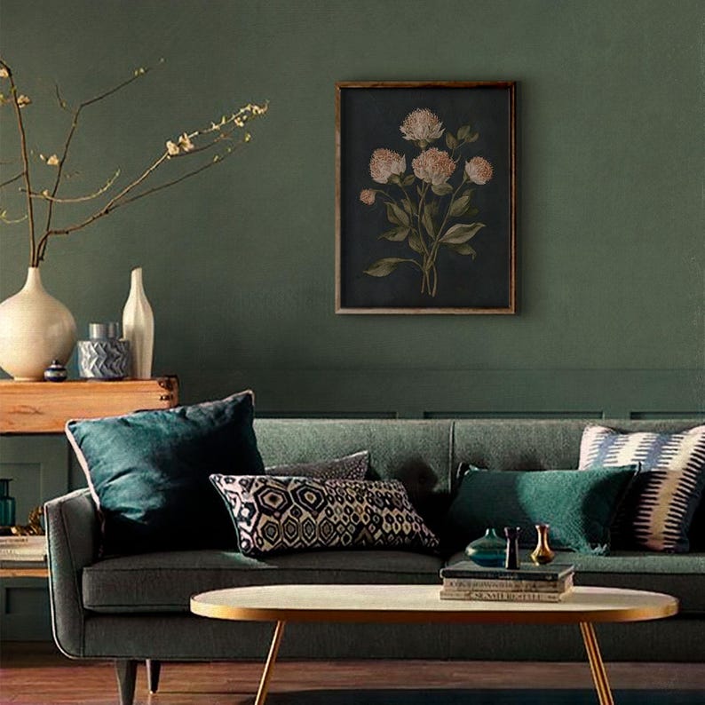 May include: A living room scene with a dark green sofa, throw pillows, and a wooden framed floral print. A gold-toned coffee table sits in front of the sofa. Decorative vases and a wooden box are on a side table. The wall is painted a dark green.