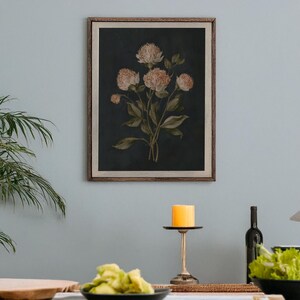 May include: A framed botanical print featuring a cluster of flowers with light peach-colored blooms and green leaves against a dark background. The artwork is in a wooden frame, adding a touch of rustic charm to the floral arrangement.