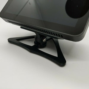 May include: A black tablet computer with a screen and a black stand. The stand is shaped like a triangle with rounded edges.