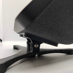 May include: A black stand with a three-pronged base and a hinged arm that can be adjusted to different angles. The stand is made of plastic and has a textured surface.