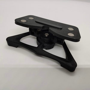 May include: A black 3D printed object with a triangular base and a top section with four circular magnets. The top section is hinged and can be folded down.