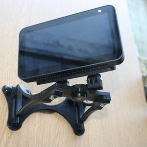 May include: A black wall mount with a swivel arm for a smart display. The display is black and has a screen with a black border. The mount is made of plastic and has a textured surface.