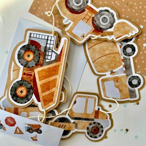Peut inclure: Une guirlande sur le thème de la construction avec divers véhicules tels qu'un camion benne, une bétonnière et un rouleau compresseur. La guirlande est faite de carton brun avec des illustrations de style aquarelle d'engins de chantier.