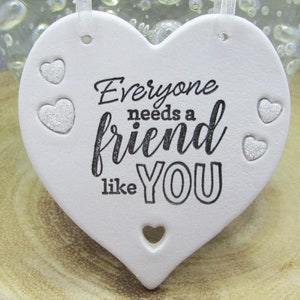 May include: White ceramic heart-shaped ornament with the text "Everyone needs a friend like YOU" in black lettering. The ornament has a glittery finish and several small silver hearts.