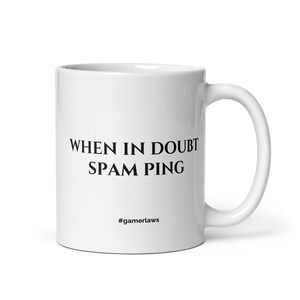 May include: White ceramic mug with a curved handle. The mug features the text "WHEN IN DOUBT SPAM PING" in black, with the hashtag "#gamerlaws" below. A gaming-themed gift.