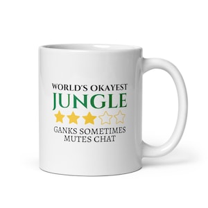 May include: White ceramic mug with the text "WORLD'S OKAYEST JUNGLE" in black and green, with three gold star icons. Below the text is "GANKS SOMETIMES MUTES CHAT". The mug has a white handle.