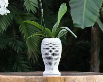 May include: A white orchid plant with white flowers in a white, textured, decorative pot. The plant is sitting on a wooden surface.