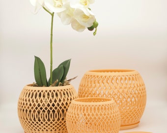 May include: Three peach-colored, open-weave, spherical planters of varying sizes. One planter holds a white orchid with green leaves. A matching saucer sits beside the smallest planter. The planters have a decorative, geometric design.