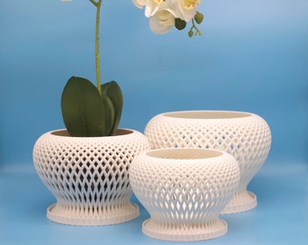 May include: Three white ceramic planters with a lattice design. The largest planter is empty, while the middle planter holds a smaller planter with a white orchid plant.