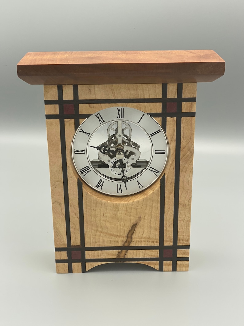 May include: A wooden clock with a silver face and Roman numeral markings. The clock is framed with a geometric design of black and brown wood with red accents.