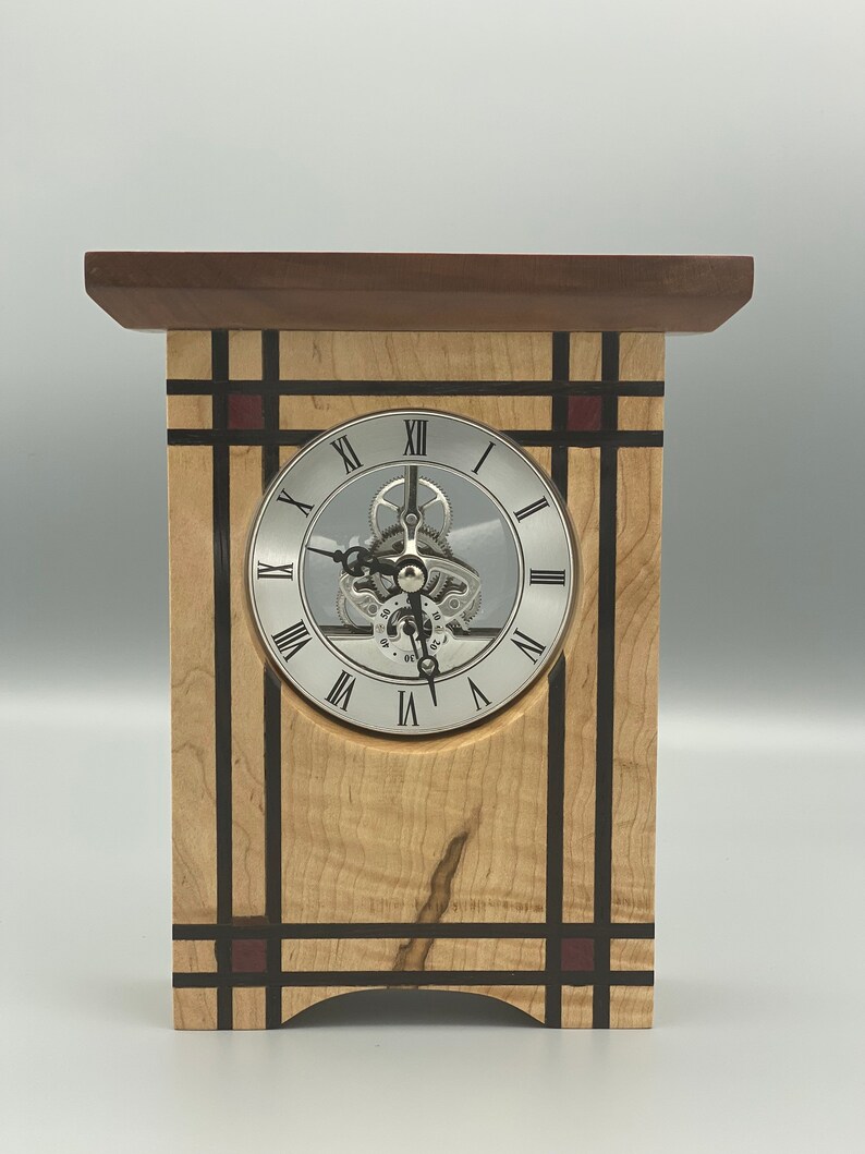 May include: A wooden clock with a silver face and Roman numeral markings. The clock is made of maple and walnut wood with black and red accents.