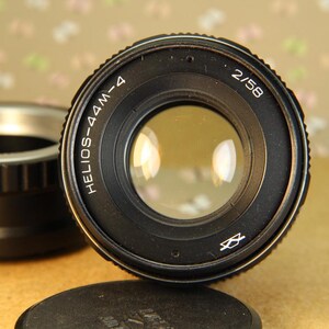 Pode incluir: Uma lente de c&acirc;mera preta com o texto "HELIOS-44M-4 2/58" impresso na lateral. A lente tem uma abertura circular e um corpo de metal preto.