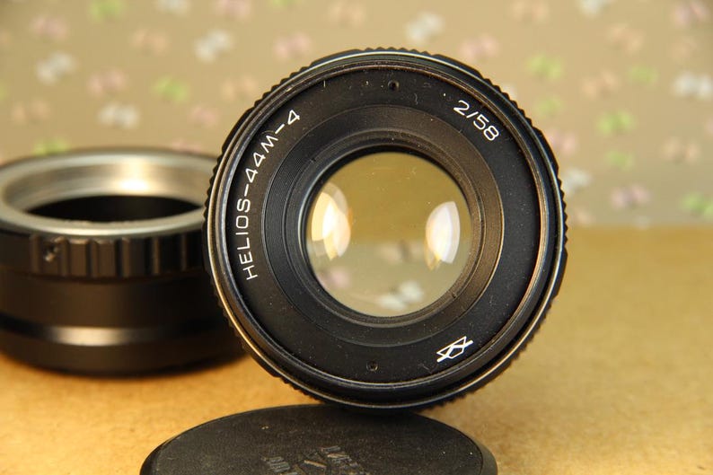 Pode incluir: Uma lente de c&acirc;mera preta com o texto "HELIOS-44M-4 2/58" impresso na lateral. A lente tem uma abertura circular e um corpo de metal preto.