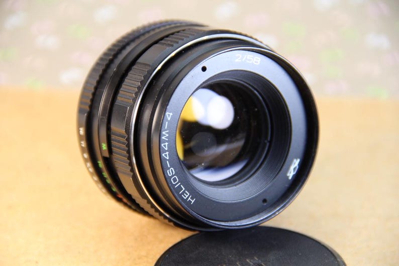 Pode incluir: Uma lente Helios-44M-4 58mm f/2 preta com um anel e marcas prateadas. A lente tem um anel de abertura preto com marcas brancas.