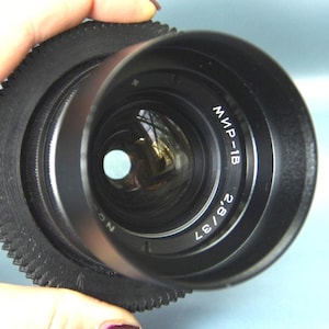 May include: A black camera lens with a gear ring and the text "Мир-1B 2.8/57" printed on the side.