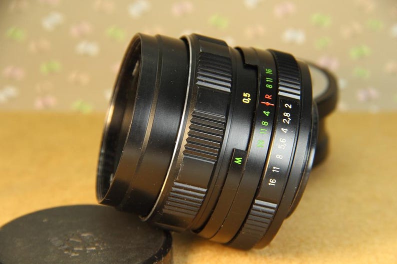 Pode incluir: Uma lente de c&acirc;mera preta com um anel prateado e um anel de abertura preto. O anel de abertura tem marcas para f/16, f/11, f/8, f/5.6, f/4, f/2.8 e f/2. A lente tamb&eacute;m tem uma escala de profundidade de campo e um anel de foco.