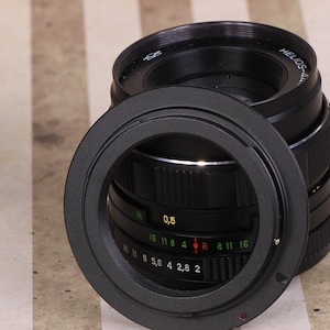 Pu&ograve; includere: Un obiettivo per fotocamera nero con un anello argentato e un tappo dell'obiettivo nero. L'obiettivo ha una scala di profondit&agrave; di campo con segni per f/2, f/2.8, f/4, f/5.6, f/8, f/11 e f/16. L'obiettivo ha anche un anello di messa a fuoco con segni per 0,5 metri, 1 metro, 1,5 metri, 2 metri, 4 metri, 8 metri, 11 metri e 16 metri.