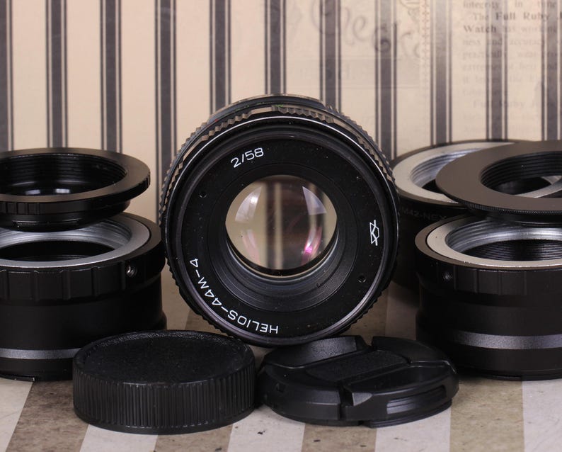 May include: A black camera lens with the text "HELIOS-44M-4" and "2/58" printed on the side. The lens is surrounded by several black metal lens adapters.