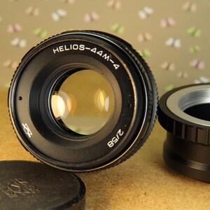 Pode incluir: Uma lente de c&acirc;mera preta com o texto "HELIOS-44M-4 2/58" impresso na lateral. A lente tem um anel prateado ao redor da frente.