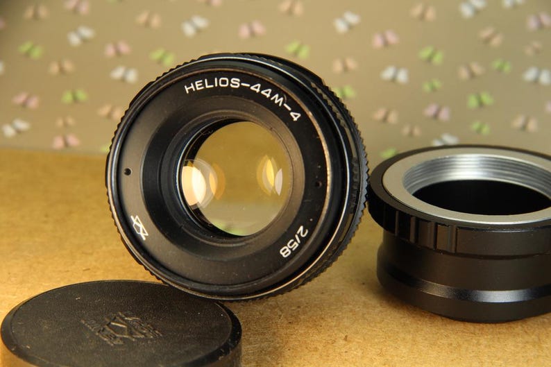 Pode incluir: Uma lente de c&acirc;mera preta com o texto "HELIOS-44M-4 2/58" impresso na lateral. A lente tem um anel prateado ao redor da frente.