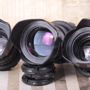 May include: Three black camera lenses with lens hoods. The lenses have different markings, including "KCI" and "МИР-1В".