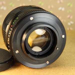 Pode incluir: Uma lente de c&acirc;mera preta com um anel prateado ao redor da borda. A lente tem uma grande abertura e uma profundidade de campo rasa.