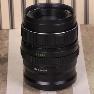 Pu&ograve; includere: Un obiettivo per fotocamera nero con un anello argentato al centro. L'obiettivo ha la scritta "M42-NEX" e "830051" stampata su di esso.