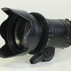 May include: A black camera lens with a lens hood and a gear ring. The lens has a white label that says "MEETEOP 5-1".