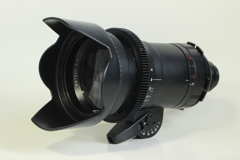 May include: A black camera lens with a lens hood and a gear ring. The lens has a white label that says "MEETEOP 5-1".