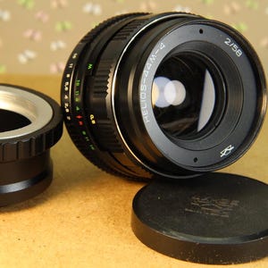 Pode incluir: Uma lente de c&acirc;mera preta com um anel prateado e o texto "HELIOS-44M-4 2/58" impresso no lado. A lente est&aacute; presa a um corpo de c&acirc;mera preto.