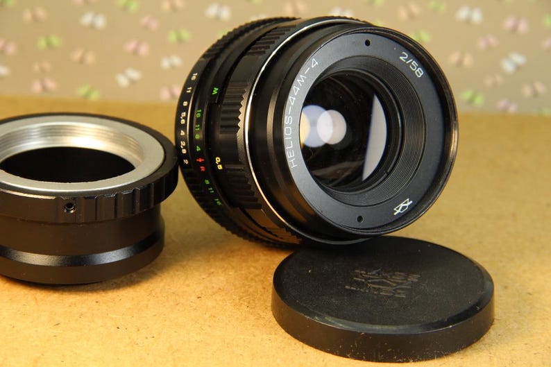 Pode incluir: Uma lente de c&acirc;mera preta com um anel prateado e o texto "HELIOS-44M-4 2/58" impresso no lado. A lente est&aacute; presa a um corpo de c&acirc;mera preto.