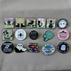 May include: A collection of 15 enamel pins featuring various designs, including a ghost, a skull, a cat, a dragon, and a jester. The pins are colourful and have a variety of themes, including spooky, cute, and funny.