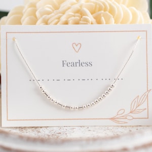 May include: A silver necklace with a delicate chain and small beads. The necklace is displayed on a white card with the word "Fearless" printed on it.
