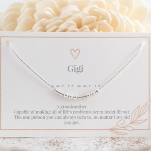 Puede incluir: Una tarjeta blanca con un collar plateado con una fila de pequeñas cuentas. La tarjeta tiene la palabra "Gigi" y el texto "Una abuela. Capaz de hacer que todos los problemas de la vida parezcan insignificantes. La única persona a la que siempre puedes recurrir, sin importar la edad que tengas."