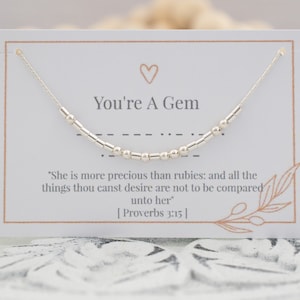 May include: A silver necklace with a beaded design, displayed on a white card. The card reads "You're A Gem" with a heart symbol and a Bible verse. The necklace is strung on a delicate chain.
