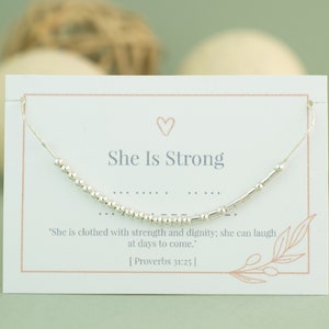 Peut inclure: Une carte blanche avec un bracelet en argent perlé sur le dessus. La carte dit "She Is Strong" et comprend une citation de Proverbes 31:25.