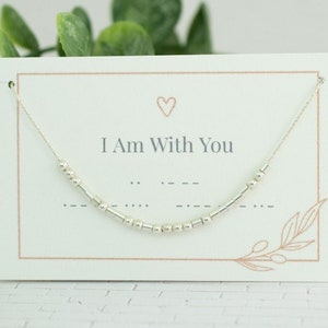 May include: A silver necklace with a small heart charm and the words "I Am With You" on a white card. The necklace is made of tiny silver beads.