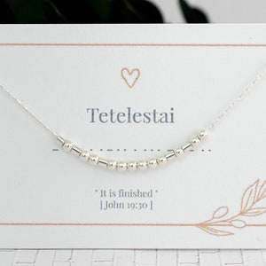 May include: A silver necklace with a delicate chain and small beads. The necklace is displayed on a white card with the word "Tetelestai" and the phrase "It is finished" [John 19:30].