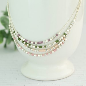 May include: A layered necklace with silver beads and small colored beads in shades of pink, green, and purple.