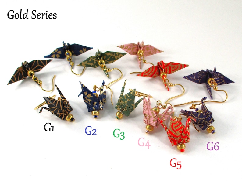 Op de afbeelding: Gold Series origami kraanvogel oorbellen in verschillende kleuren en patronen, waaronder zwart en goud, blauw en goud, groen en goud, roze en goud, rood en goud en paars en goud.