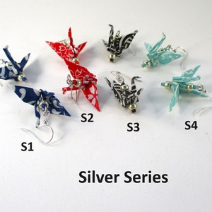 Op de afbeelding: Een set van zes origami-kraanvogel oorbellen in een zilveren serie. De oorbellen zijn gemaakt van stof en hebben verschillende patronen en kleuren, waaronder rood, blauw, zwart en wit. De oorbellen zijn gemarkeerd met S1, S2, S3 en S4.