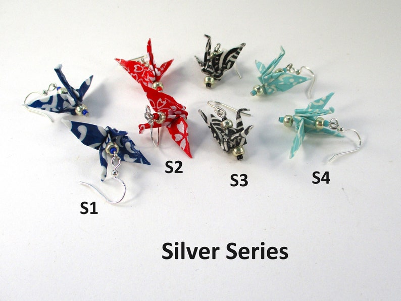 Op de afbeelding: Een set van zes origami-kraanvogel oorbellen in een zilveren serie. De oorbellen zijn gemaakt van stof en hebben verschillende patronen en kleuren, waaronder rood, blauw, zwart en wit. De oorbellen zijn gemarkeerd met S1, S2, S3 en S4.